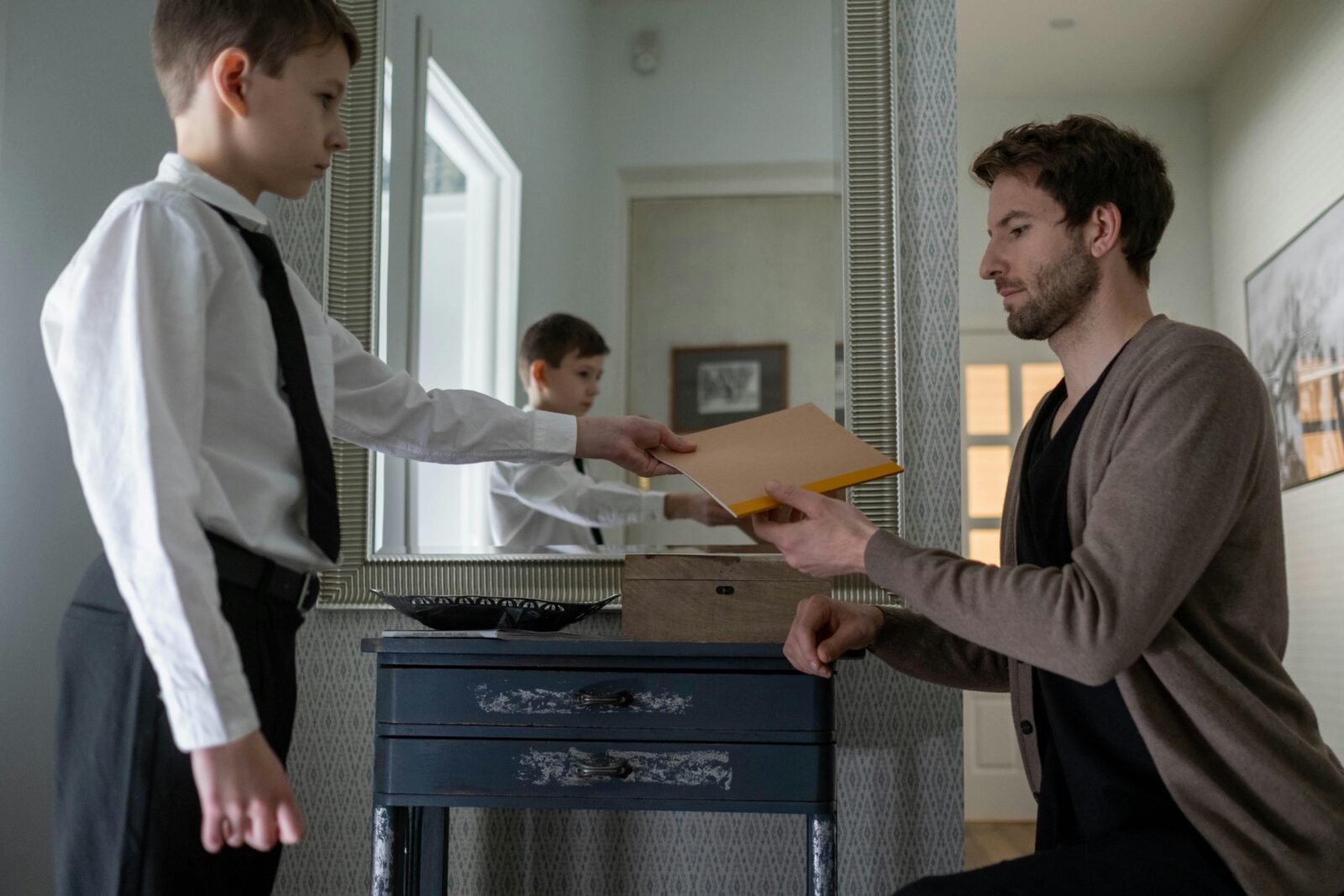 A father and son exchanging an envelope in an indoor setting, reflecting parenthood and communication.